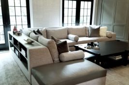 Elegant grey custom upholstered L shaped sectional with bolster pillows and a built in custom bookcase attached to the back of the sectional. \r\nInteriors: Ginger Surasky\r\nUpholstery: Bespoke by Luigi Gentile